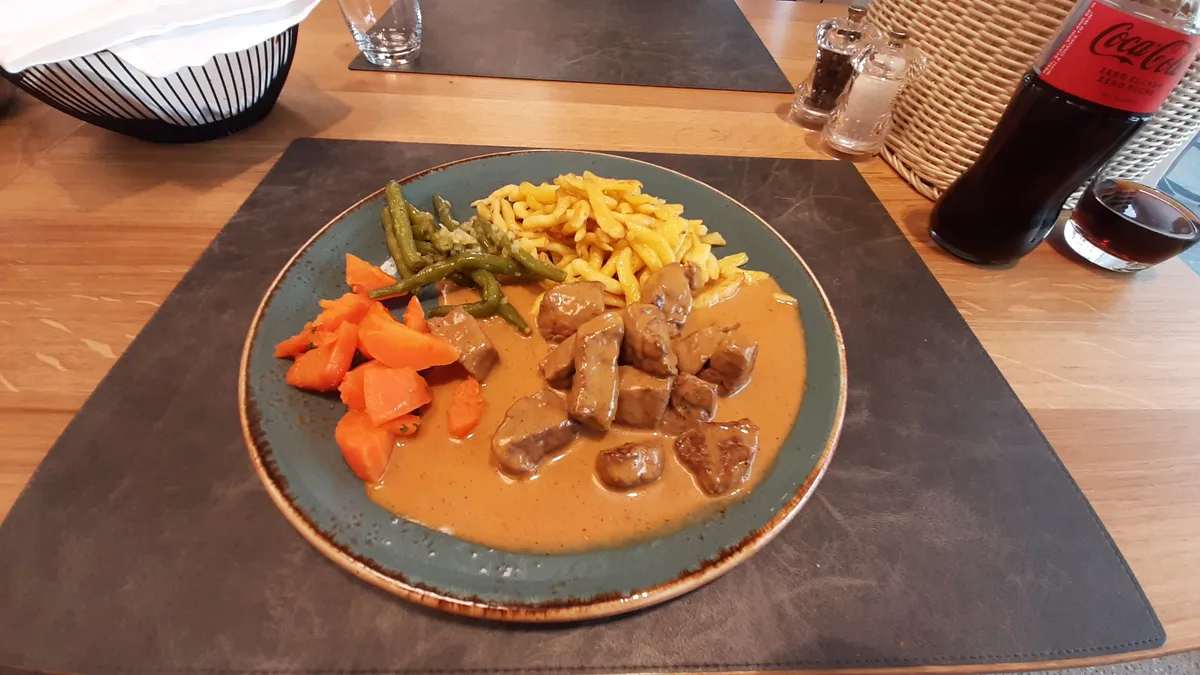 Ein Teller mit Fleisch, Sauce, Spätzli und Gemüse.